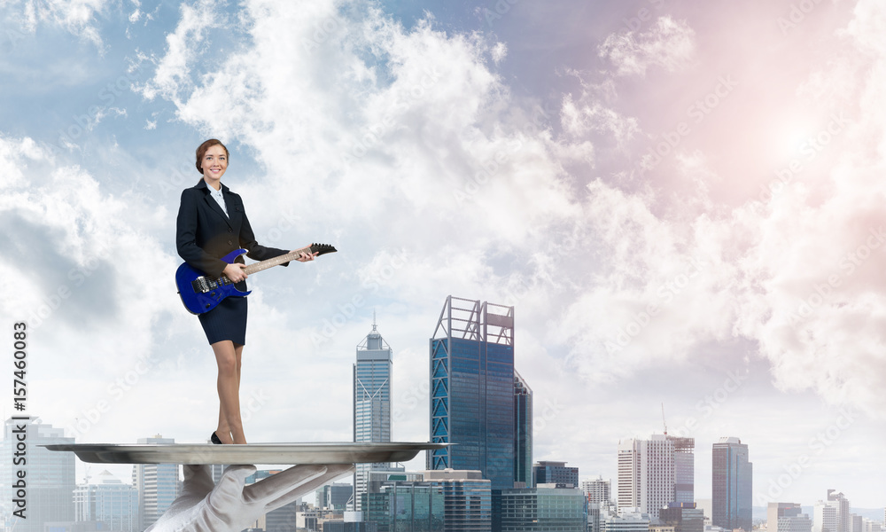 Attractive businesswoman on metal tray playing electric guitar against cityscape background