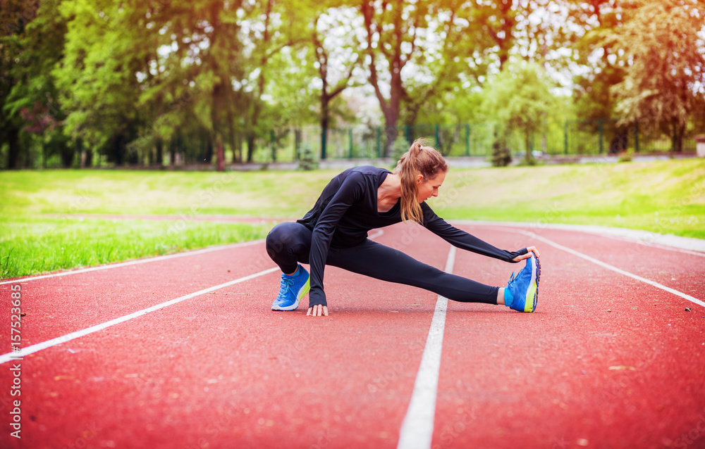 Athletic woman stretching on running track before training, healthy lifestyle