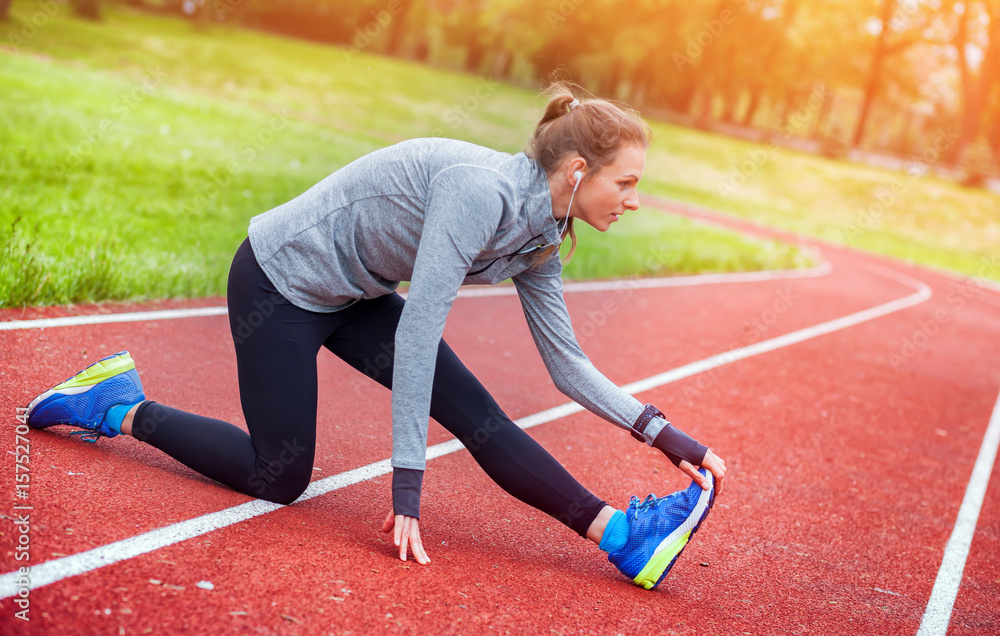 Athletic woman on running track stretching before training fitness accessories