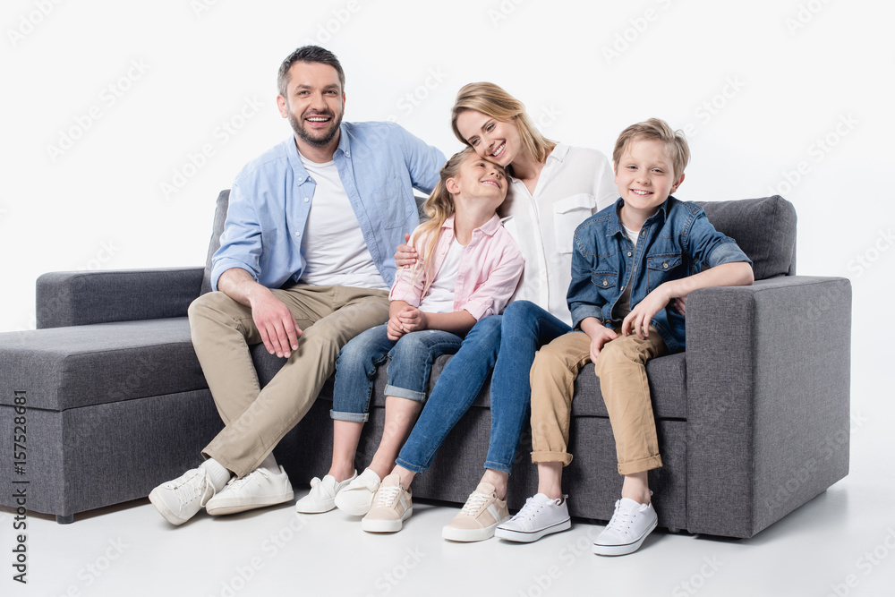 Happy young family with two children sitting together on couch isolated on white