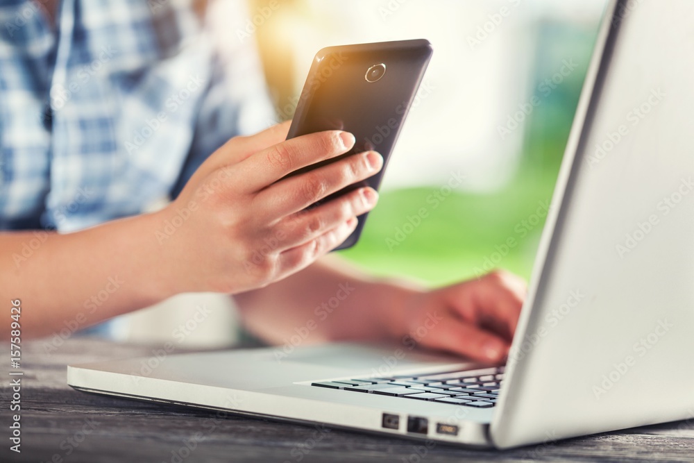 Human with phone works on laptop.