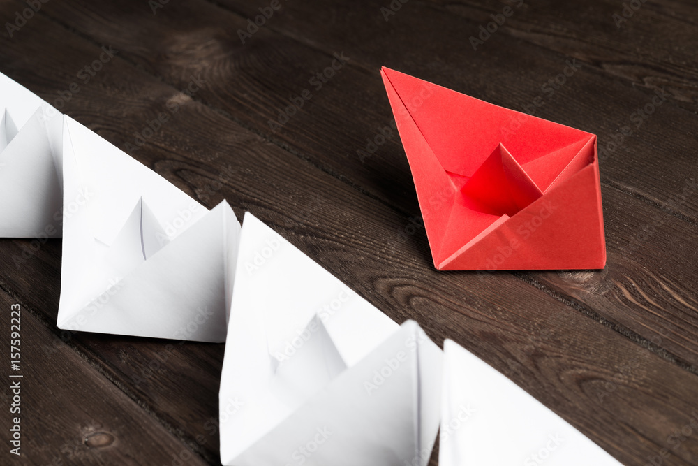 Business leadership concept with white and color paper boats on wooden table