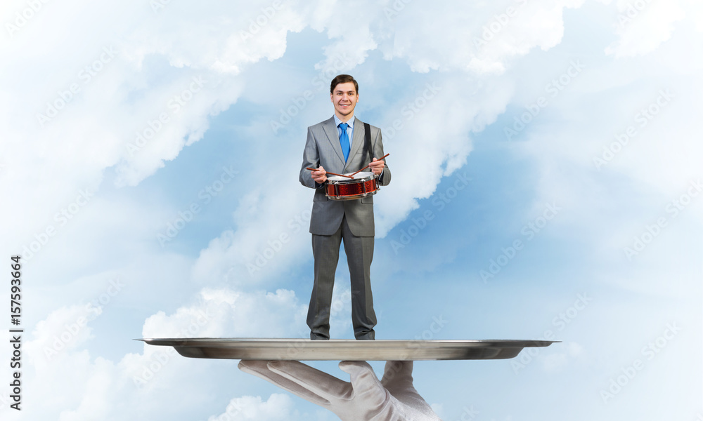 Businessman on metal tray playing drum blue sky background