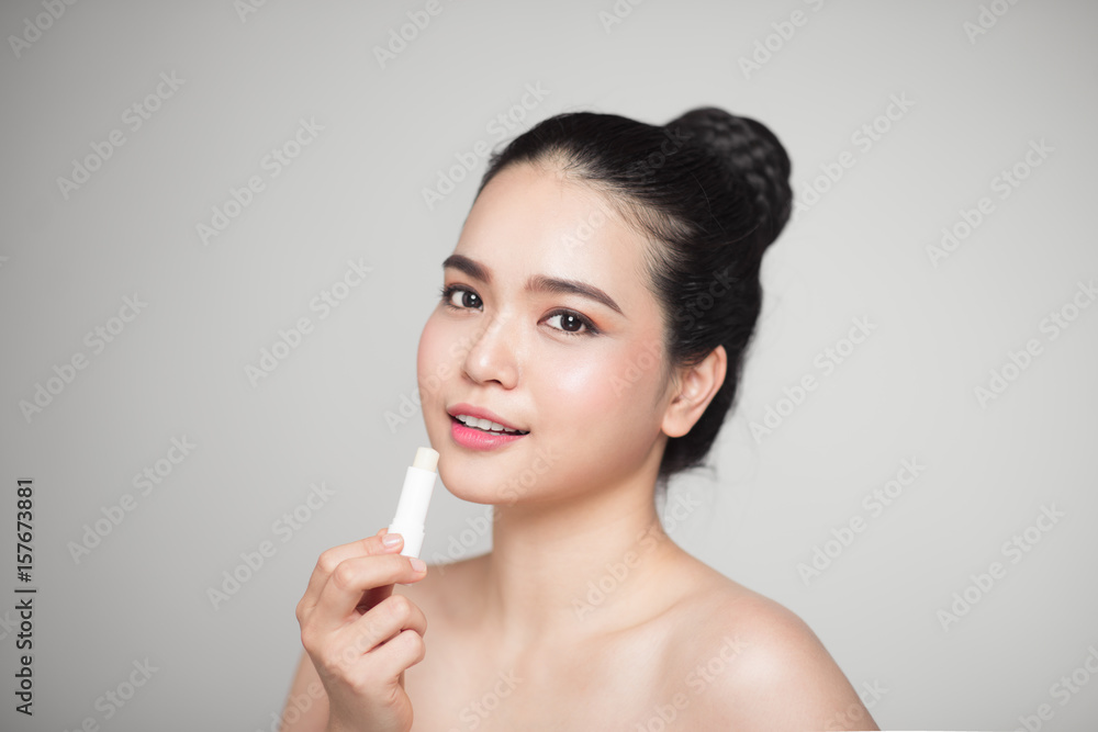 Asian woman applying hygienic lip balm over grey background