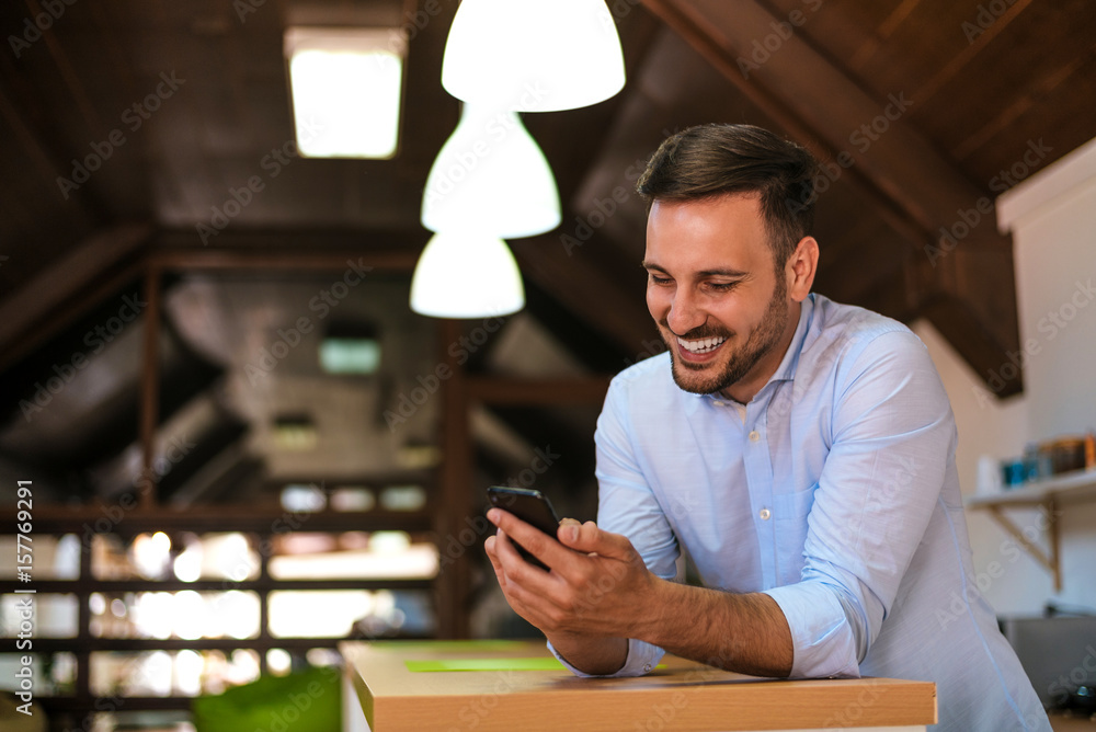 Young businessman using mobile phone while leaning on table at home