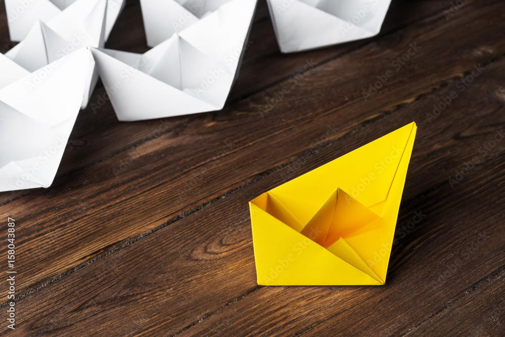 Business leadership concept with white and color paper boats on wooden table