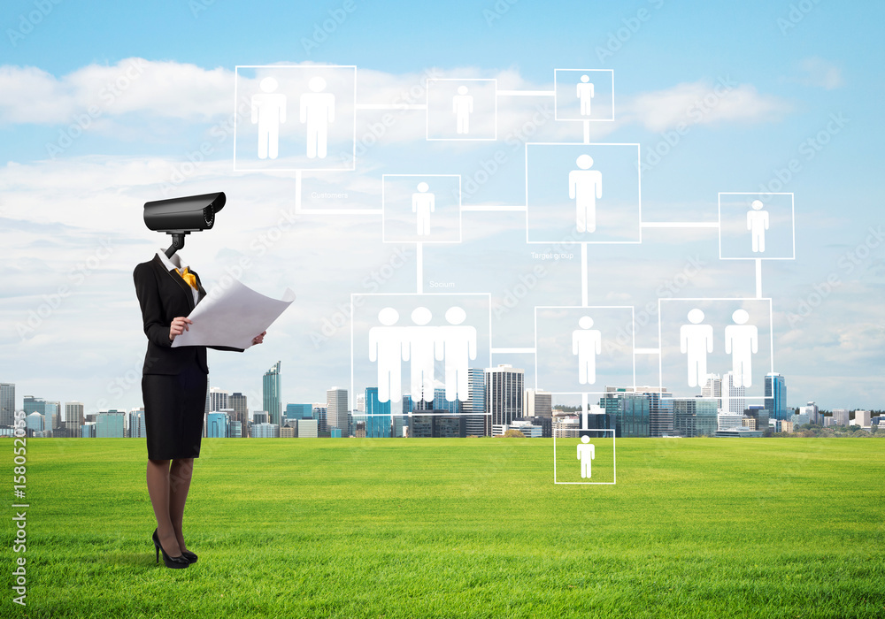 Camera headed woman standing on green grass against modern cityscape