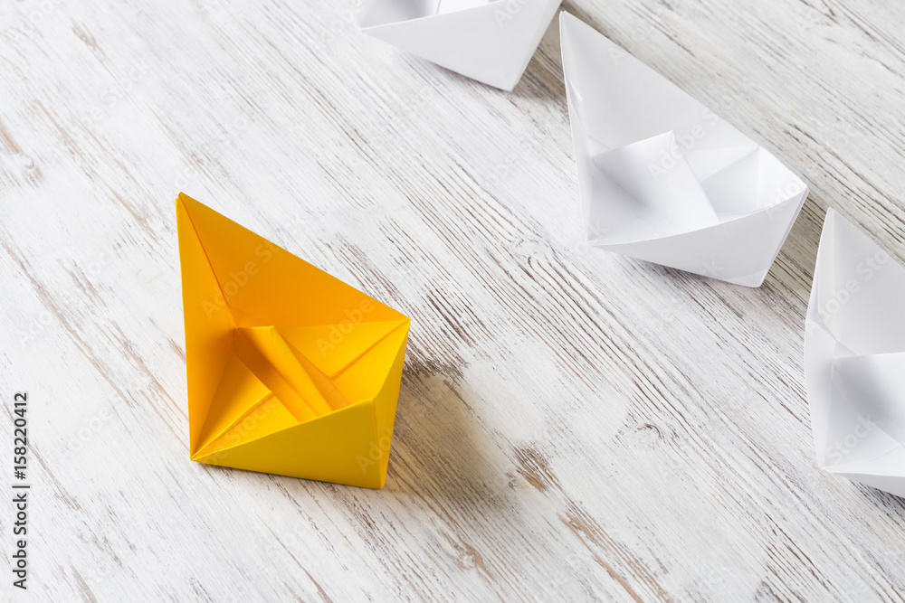 Business leadership concept with white and color paper boats on wooden table