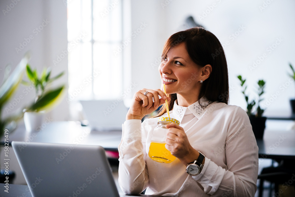 Young woman working with laptop and drinking orange juice