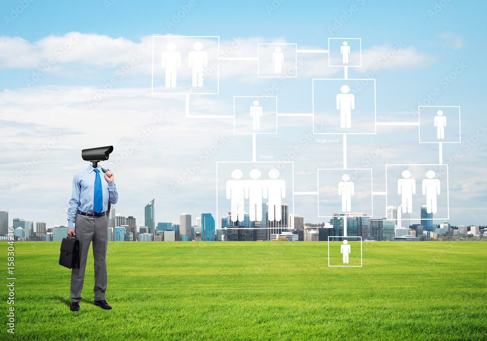 Camera headed man standing on green grass against modern cityscape