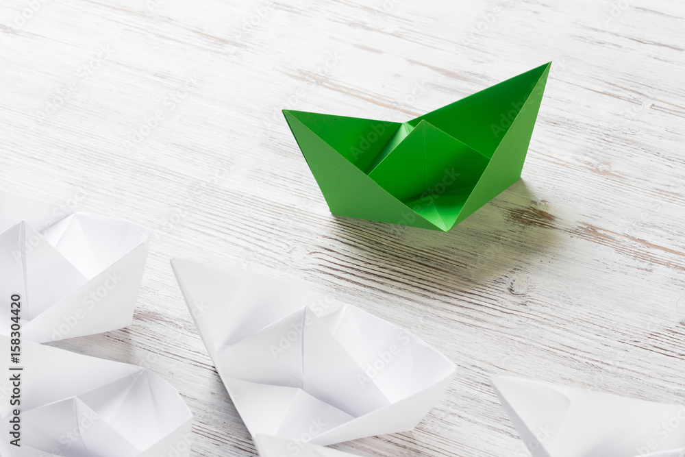 Business leadership concept with white and color paper boats on wooden table