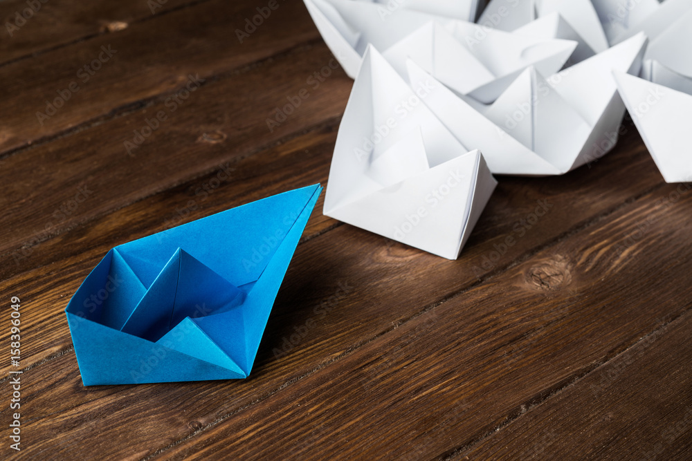 Business leadership concept with white and color paper boats on wooden table