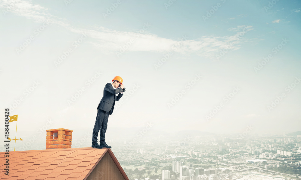 Engineer man standing on roof and looking in binoculars. Mixed m