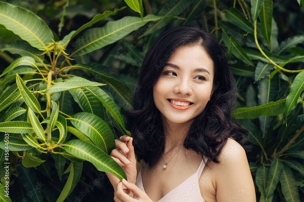 Portrait of pretty young woman standing near leaves outdoors