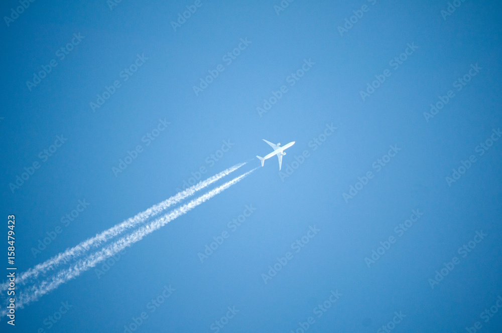 White jet plane flies high in the blue sky and leaves behind a white contrail