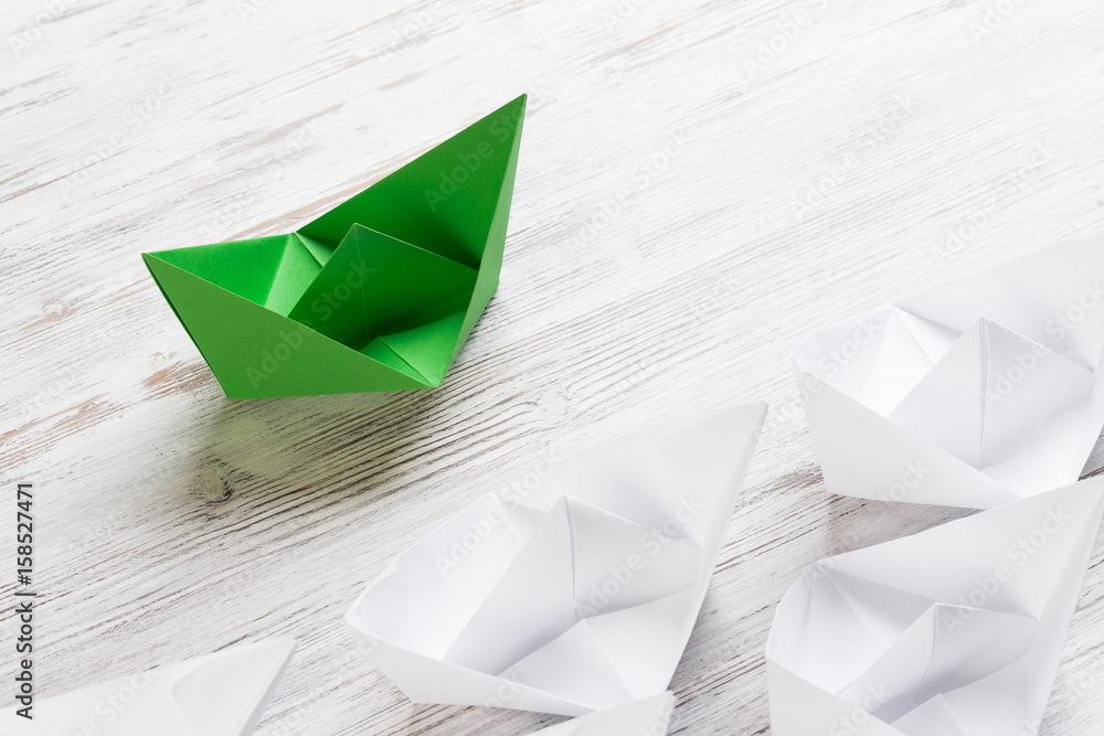 Business leadership concept with white and color paper boats on wooden table