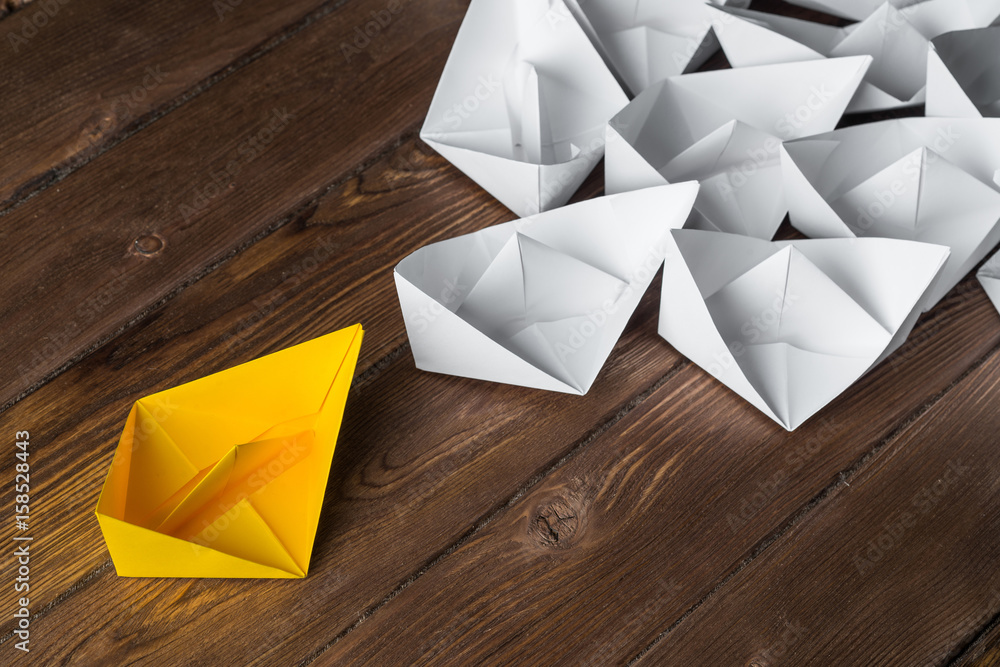 Business leadership concept with white and color paper boats on wooden table