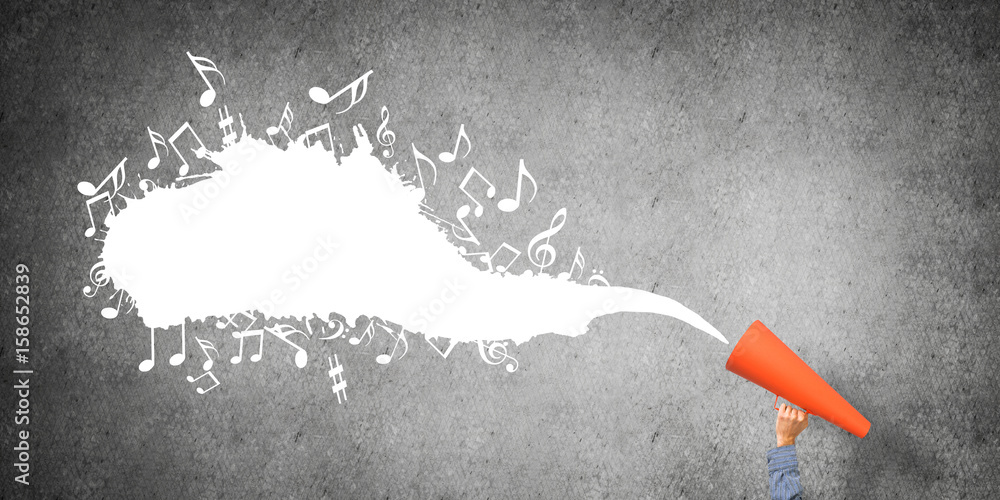 Hand of man holding orange paper trumpet against concrete background