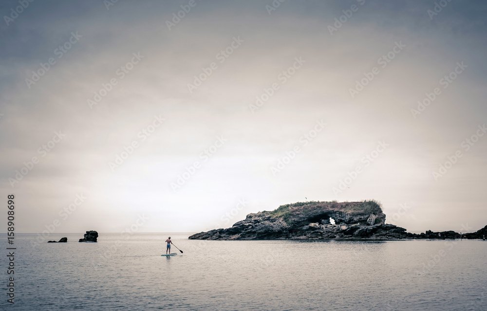 Stehpaddler im Meer vor einer Insel bei Sonnenuntergang