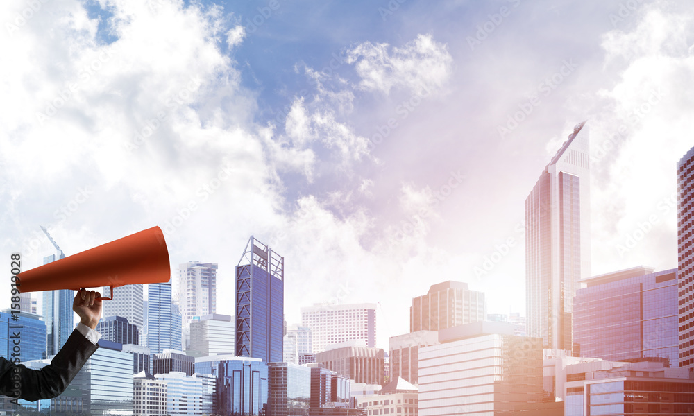 Hand of businesswoman holding red paper trumpet against cityscape background