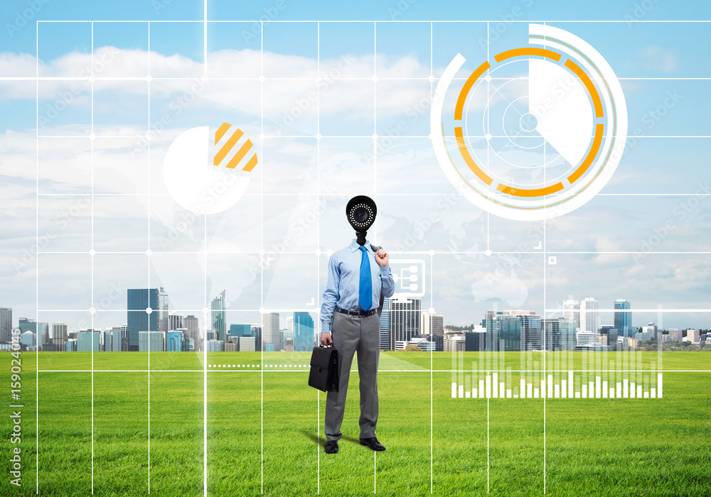 Camera headed man standing on green grass against modern cityscape