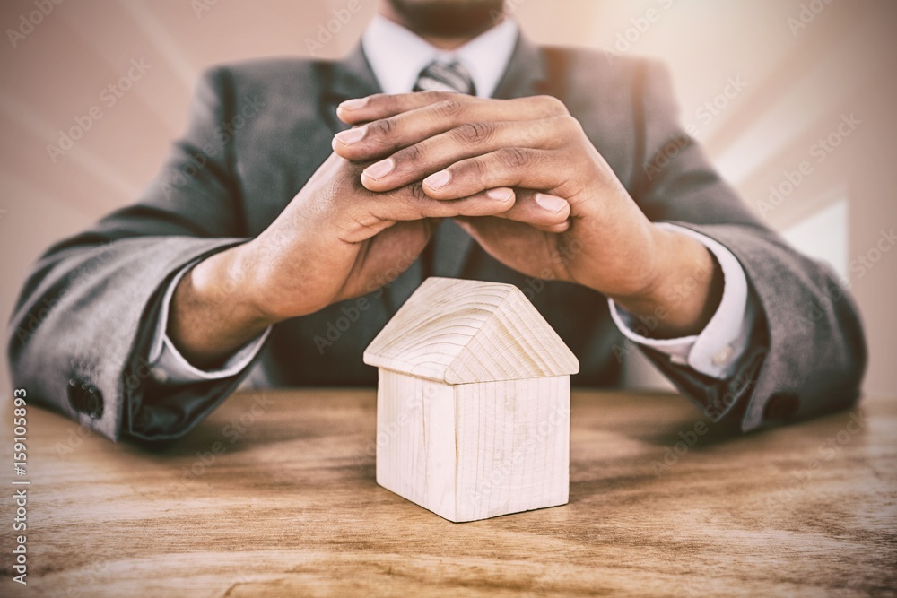 Composite image of businessman protecting house model with hands