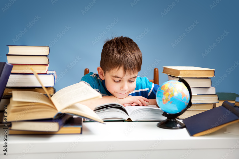 seven years old child reading a book at home. Boy studying at table on blue background