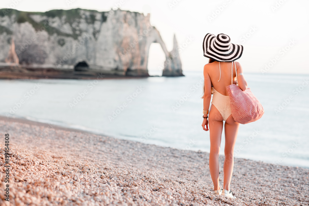 Woman in hat and swimsuit standing back with beach bag enjoying great view on the ocean during the s