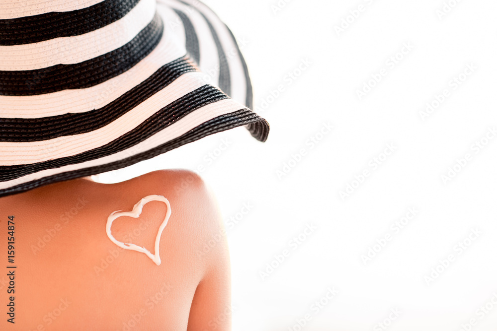 Close-up back view on a beautiful woman in striped hat with sunscreen heart shape on her shoulder on