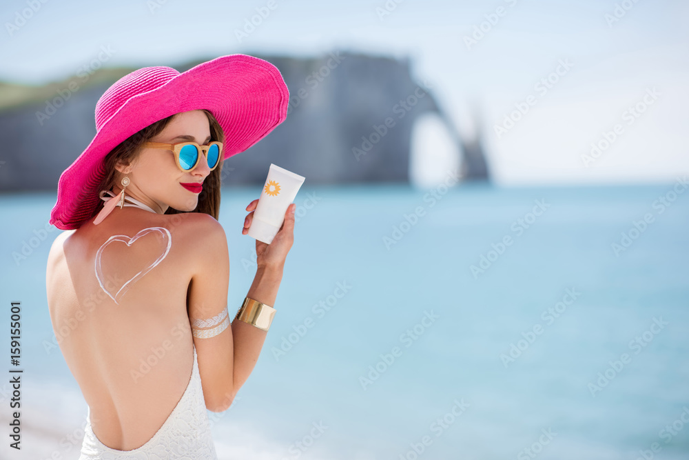 Portrait of a beautiful smiling woman in pink hat with sunscreen heart shape on her shoulder holding