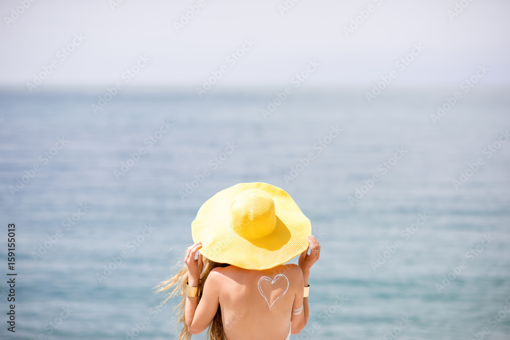 Back view on the woman in yellow hat standing on the beach on the blue water backround