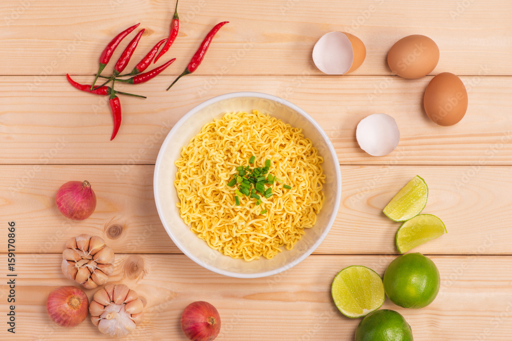 Instant noodles in bowl with vegetables on wood background