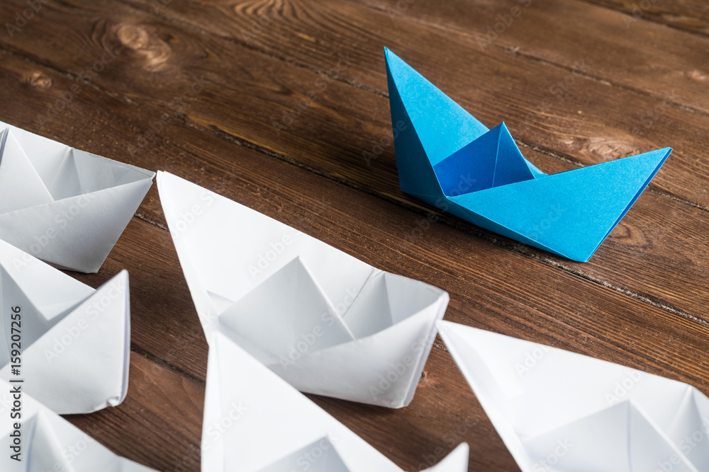 Business leadership concept with white and color paper boats on wooden table