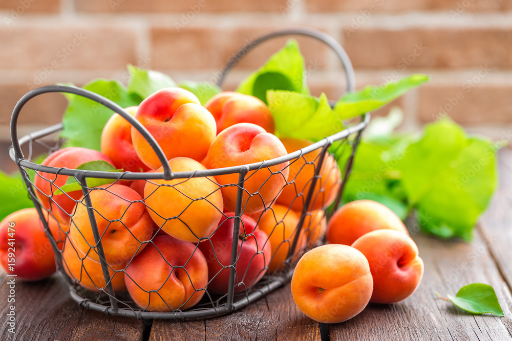 Fresh apricots with leaves in basket on wooden table