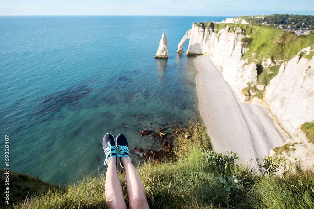 Woman in sports sneakers sitting on the cliff above the ocean with beautiful view on the rocky coast