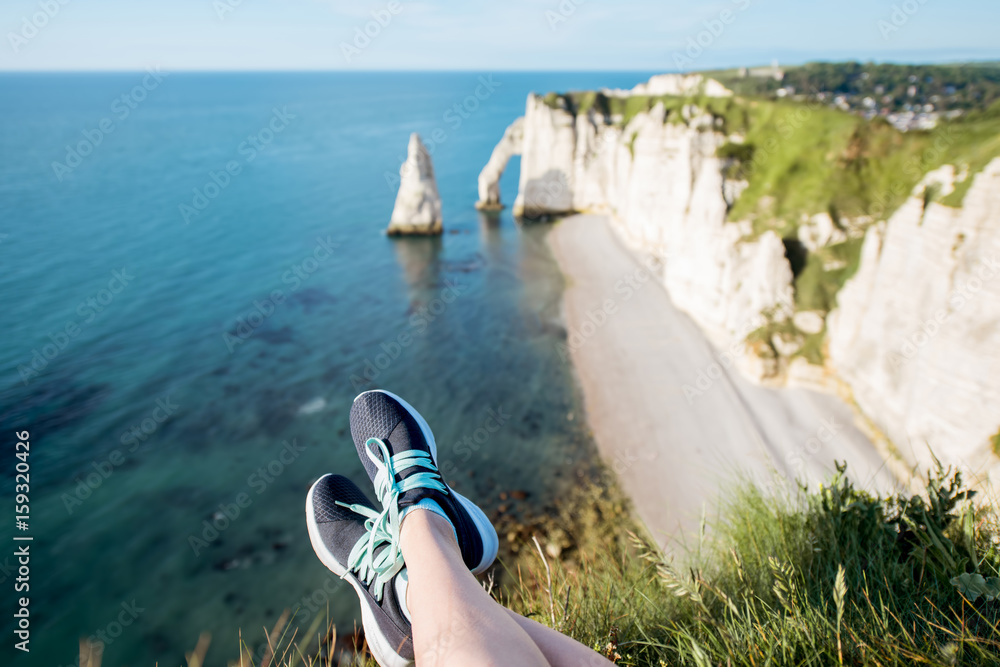 Woman in sports sneakers sitting on the cliff above the ocean with beautiful view on the rocky coast