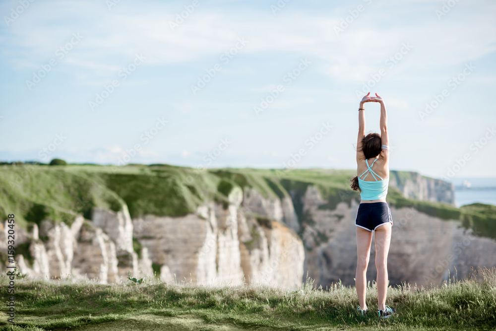 Young woman in sportswear streching outdoors on the beautiful rocky coastline background near Etreta