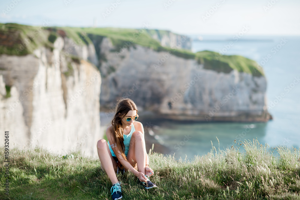 穿着运动服系鞋带的年轻女子坐在美丽的岩石海岸线上