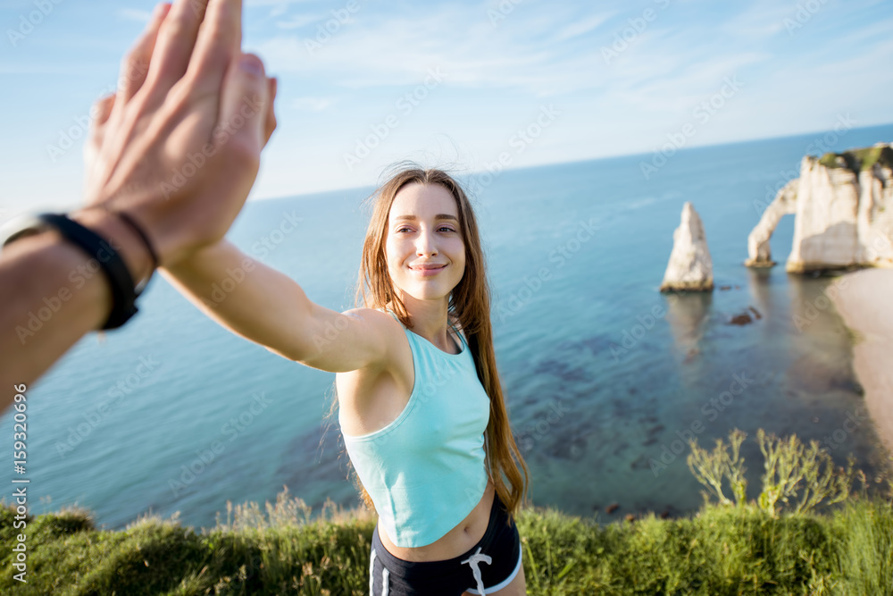 Happy playful woman in sportswear giving a five outdors on the rocky coastline background