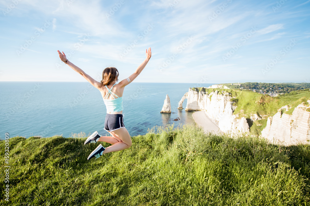 Young playful woman in sportswear jumping outdors on the beautiful rocky coastline background near E