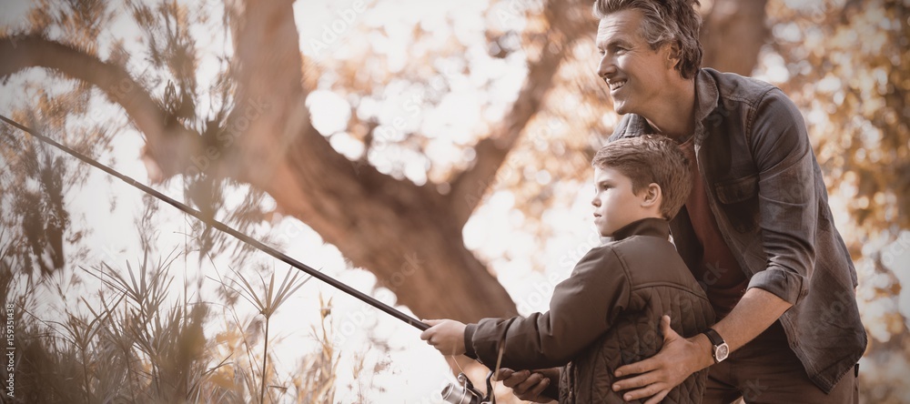 Smiling father assisting son while fishing in forest