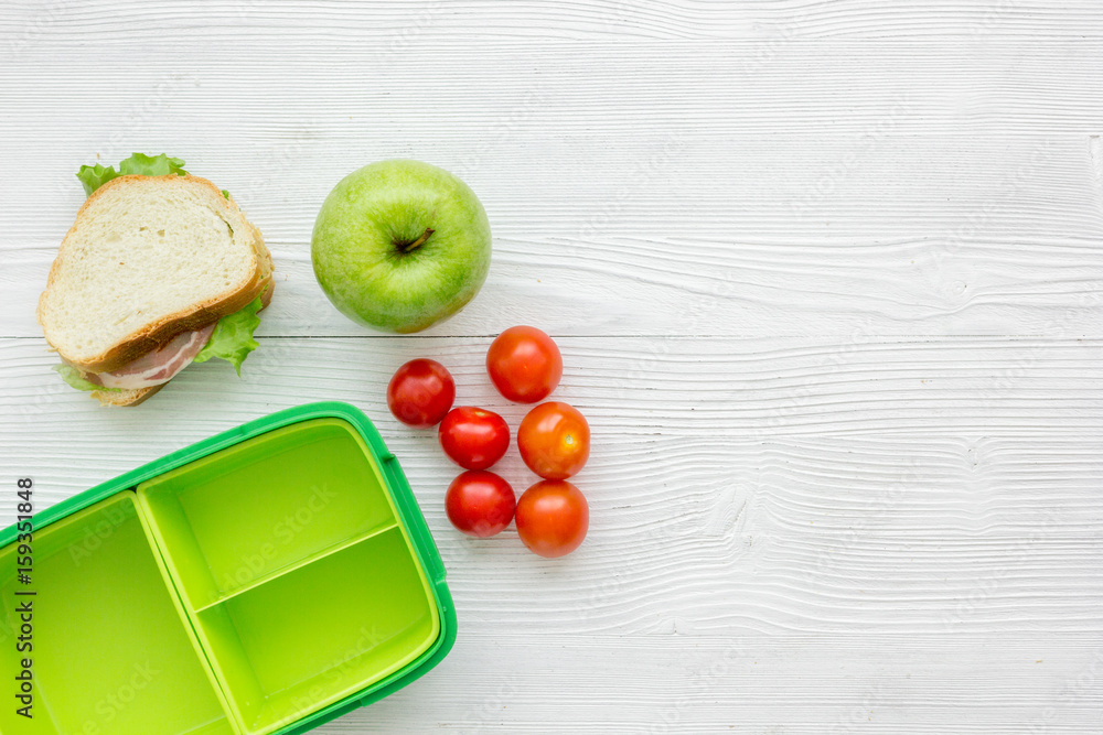 homemade lunch with apple, tomato and sandwich in green lunchbox top view mockup