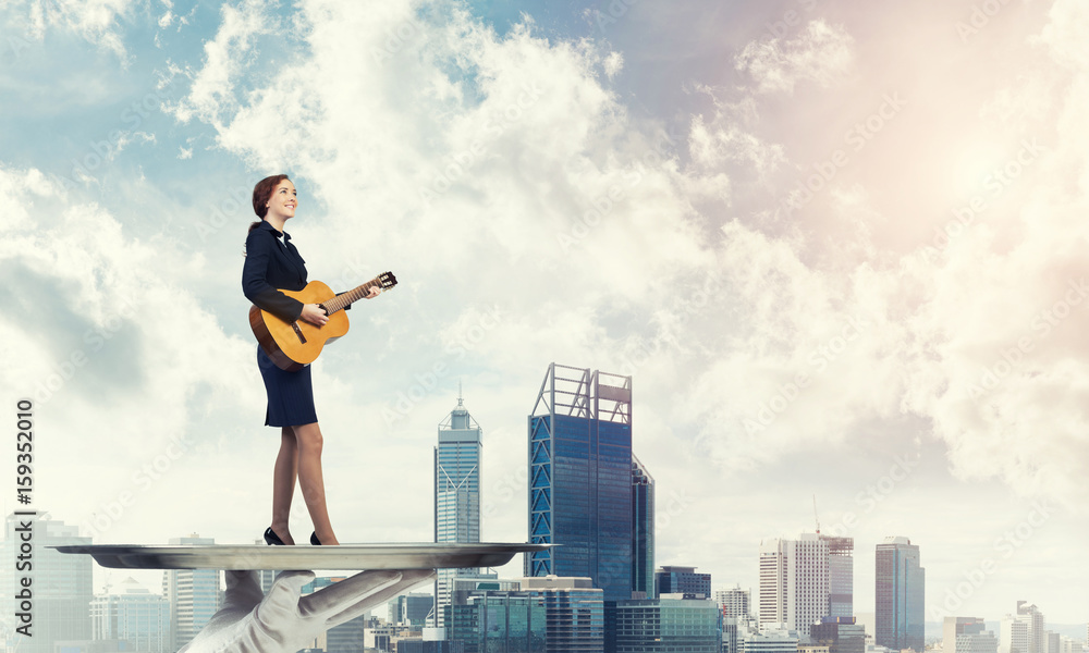 Attractive businesswoman on metal tray playing acoustic guitar against cityscape background