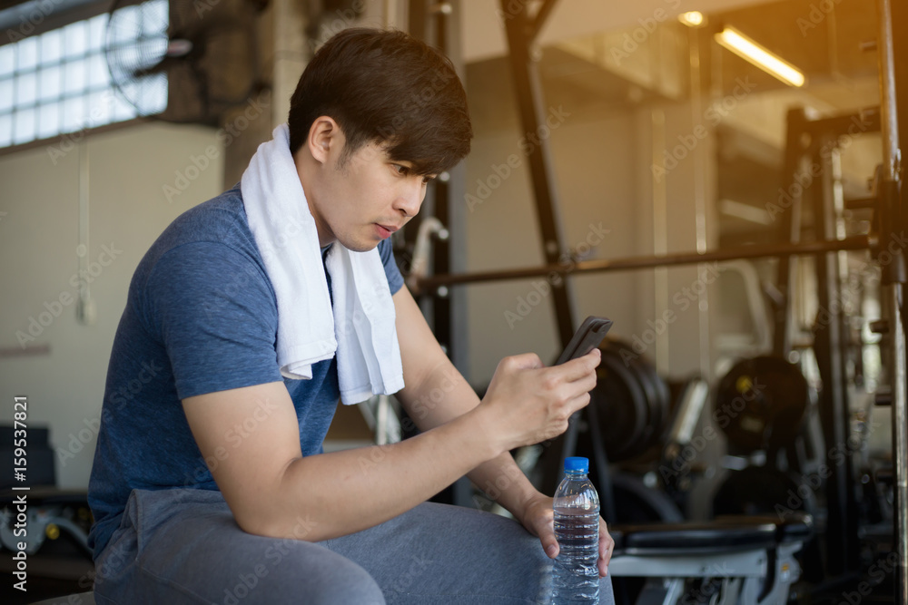 亚洲年轻男子锻炼后在健身馆使用手机