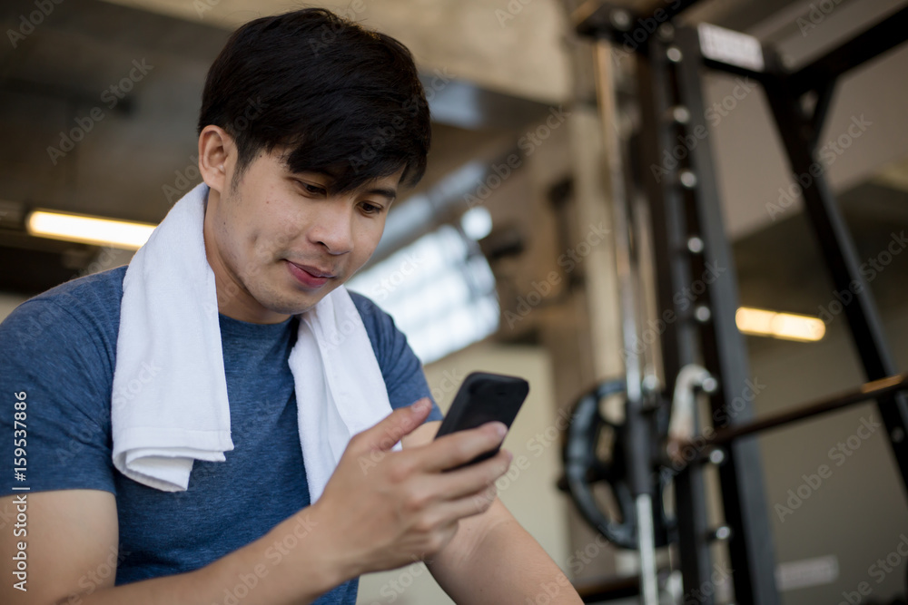 Young Asian man using mobile phone in the fitness gym after work out training