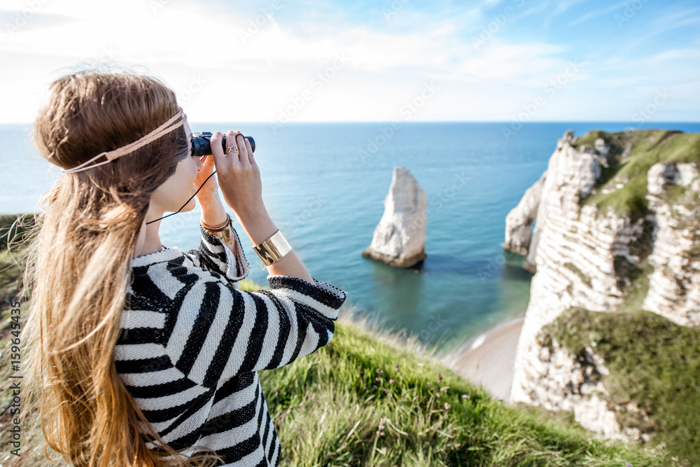 Young woman watching with binoculars on the famous rocky coastline near Etretat town in France