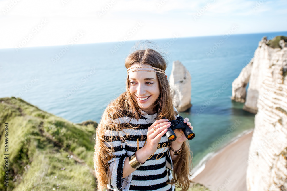 Young woman watching with binoculars on the famous rocky coastline near Etretat town in France