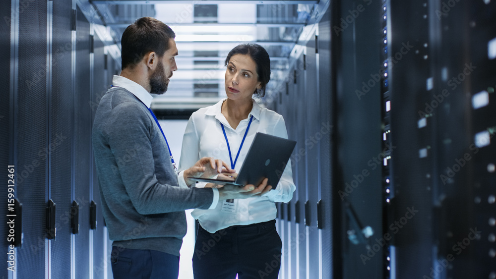 Male IT Specialist Holds Laptop and Discusses Work with Female Server Technician. Theyre Standing i