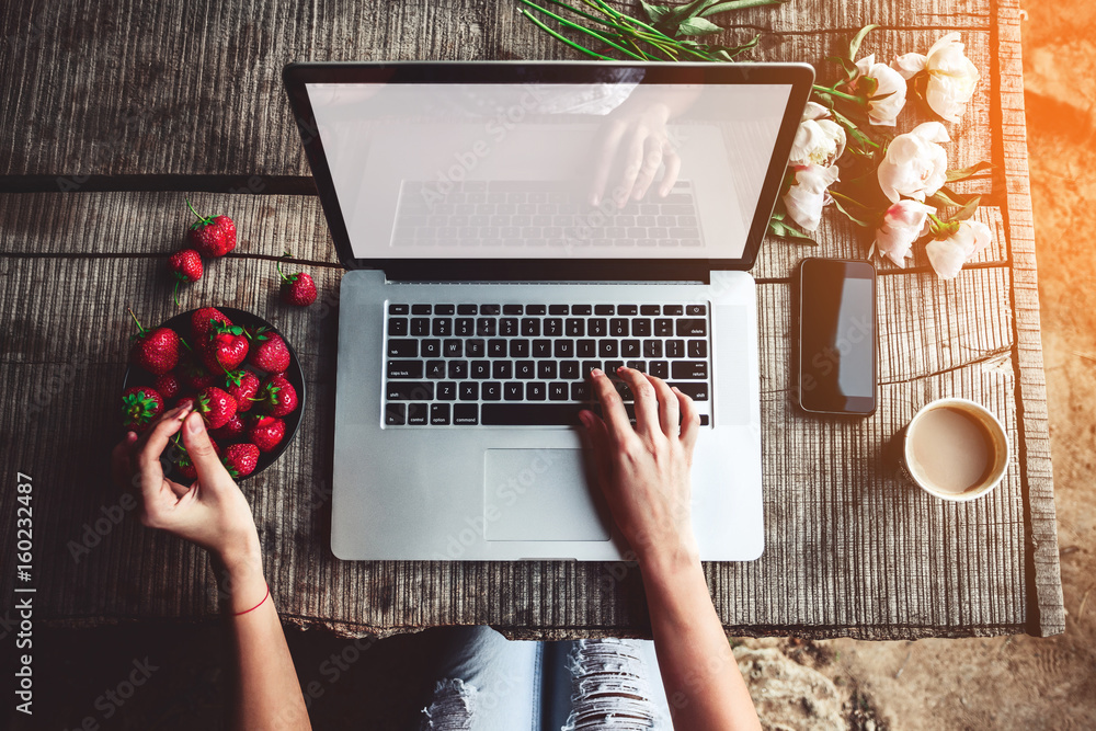 Workspace with girls hands, laptop computer, bouquet of peonies flowers, coffee, strawberries, smar