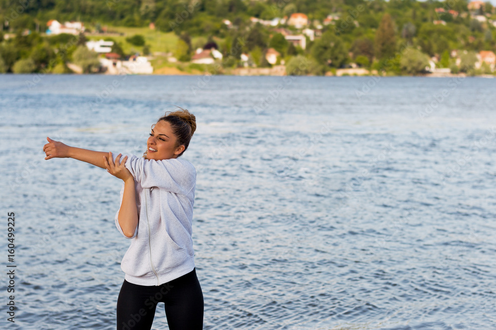 Portrait of smiling young athlete woman preparing for a workout outdoors near the river.